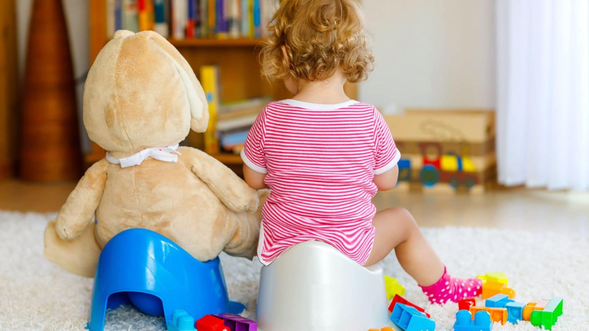 Bebé sentada en orinal con peluche de oso.