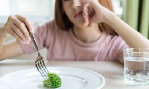 Adolescente delante de un plato con un trozo de brócoli