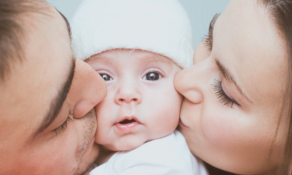 Padres besando la cara de un bebé