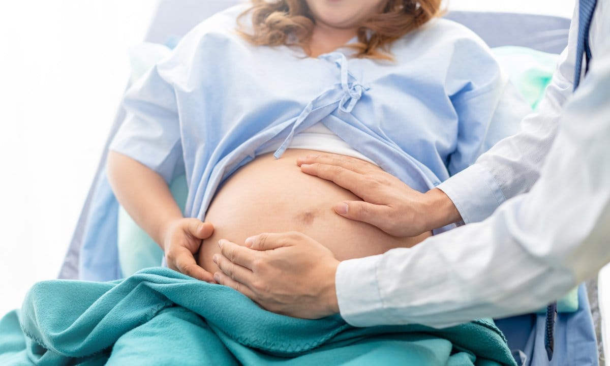 Médico toca la tripa de mujer embarazada tumbada en una camilla