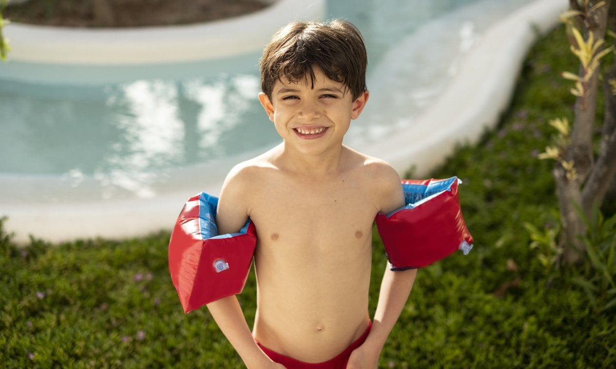 Niño con manguitos en la piscina en verano.