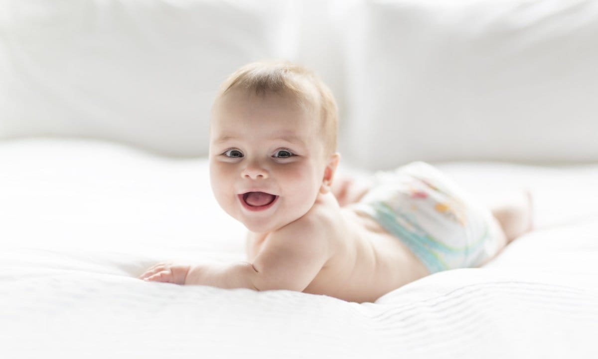 Bebé sobre la cama girándose y sonriente