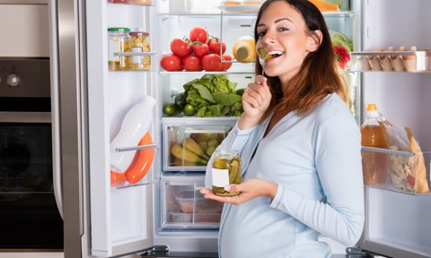 Mujer embarazada comiendo con la nevera abierta.