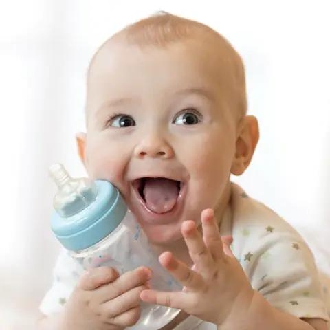 Bebé sonriendo con biberón. Lactancia.