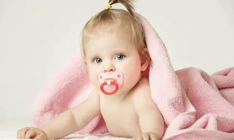 Bebé niña tumbada con chupete rosa y toalla.