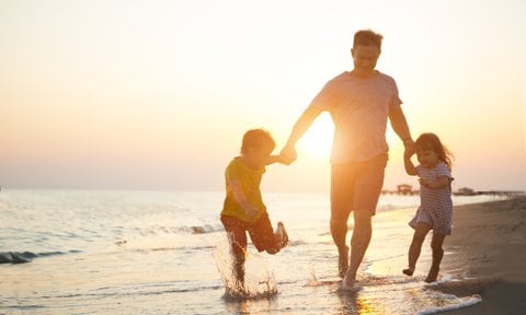Padre con dos hijos en la playa al atardecer