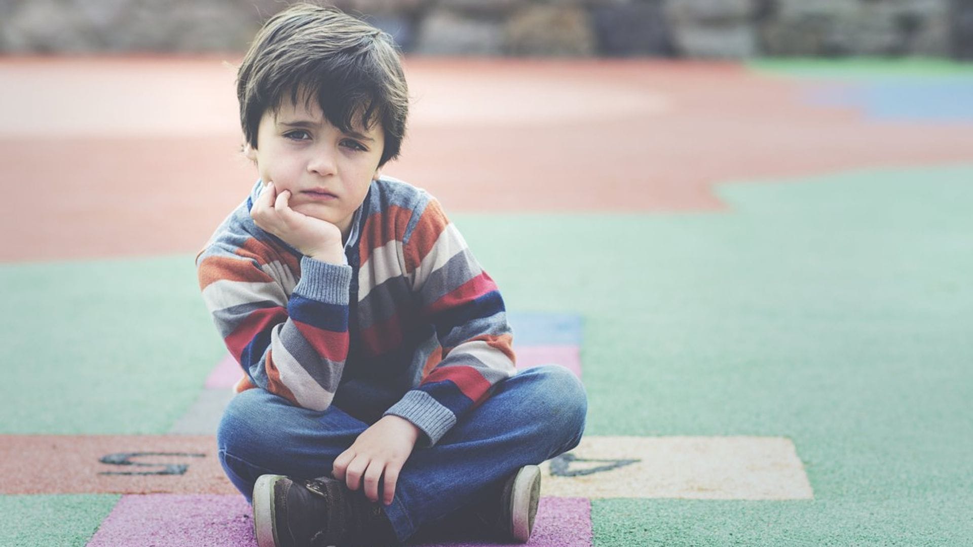 Niño triste en el patio del colegio, sin amigos.