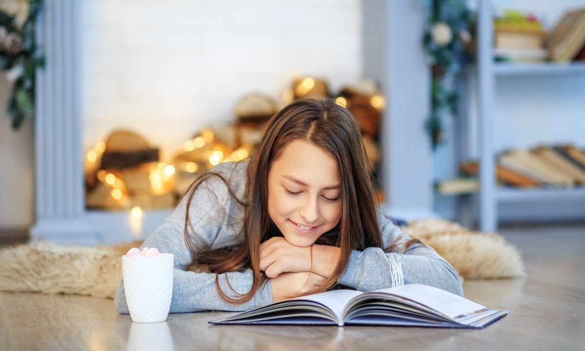 Chica adolescente leyendo en el suelo en Navidad