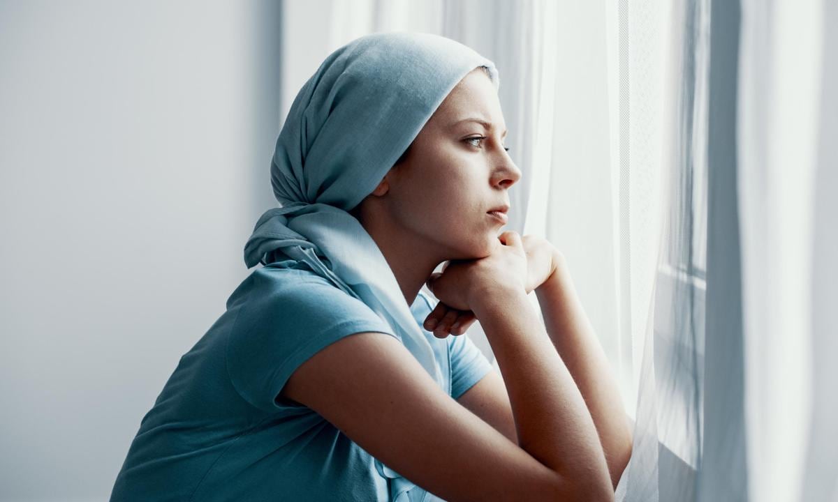 Chica adolescente con cáncer mirando por la ventana