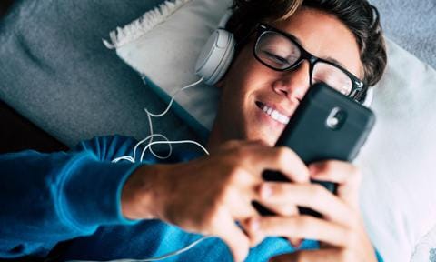 Adolescente con móvil tirado en la cama