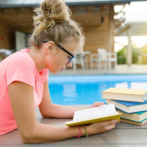 Adolescente leyendo en la piscina en verano.