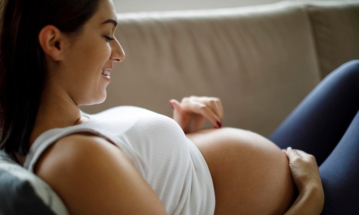 Mujer embarazada en el sofá tocándose la tripa