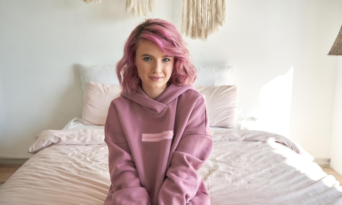 Adolescente sentada en la cama con el pelo pintado de rosa