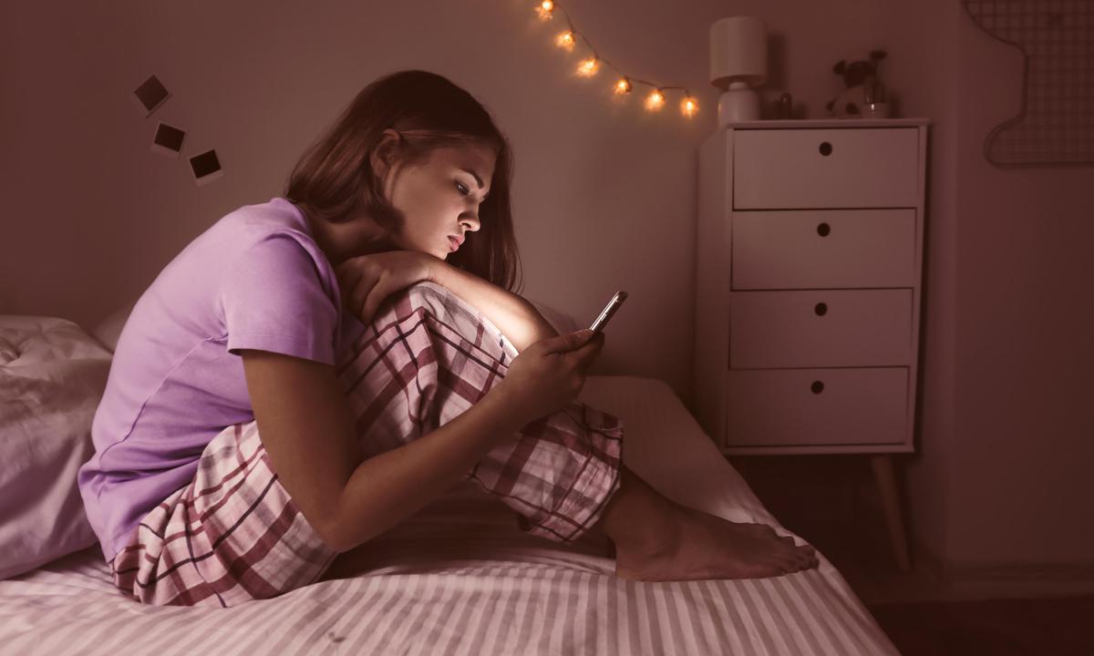 Adolescente consultando el móvil por la noche en la cama