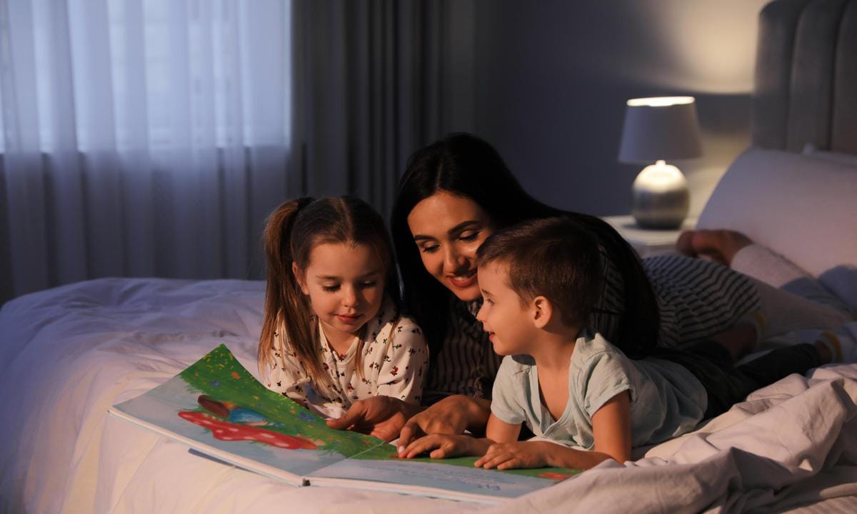 Madre leyendo un cuento a sus hijos tumbados en la cama de su habitación