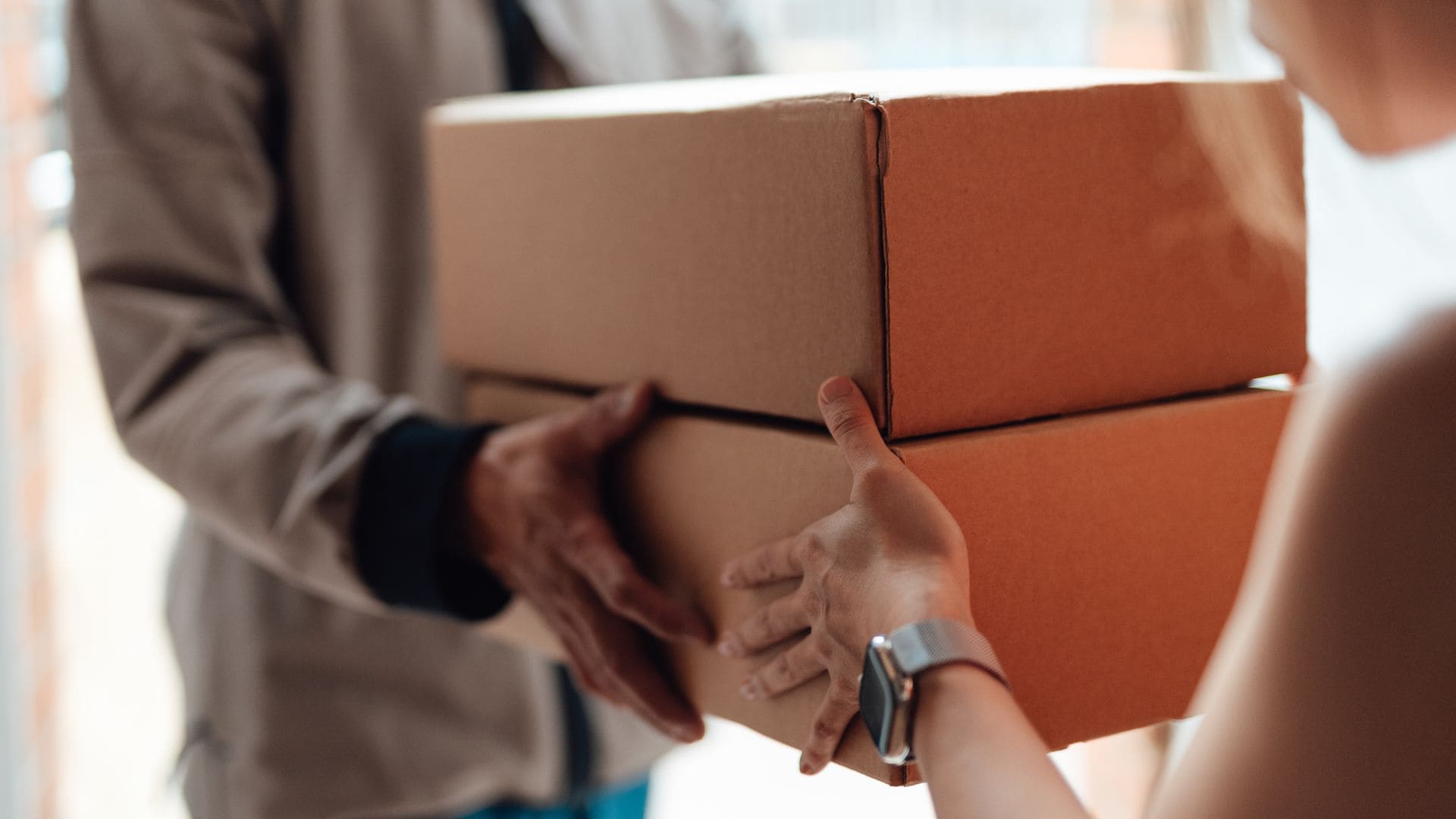 Cropped shot of courier person standing at front door, handing over a parcel to customer. Door to door courier service. Express delivery and online shopping. 
