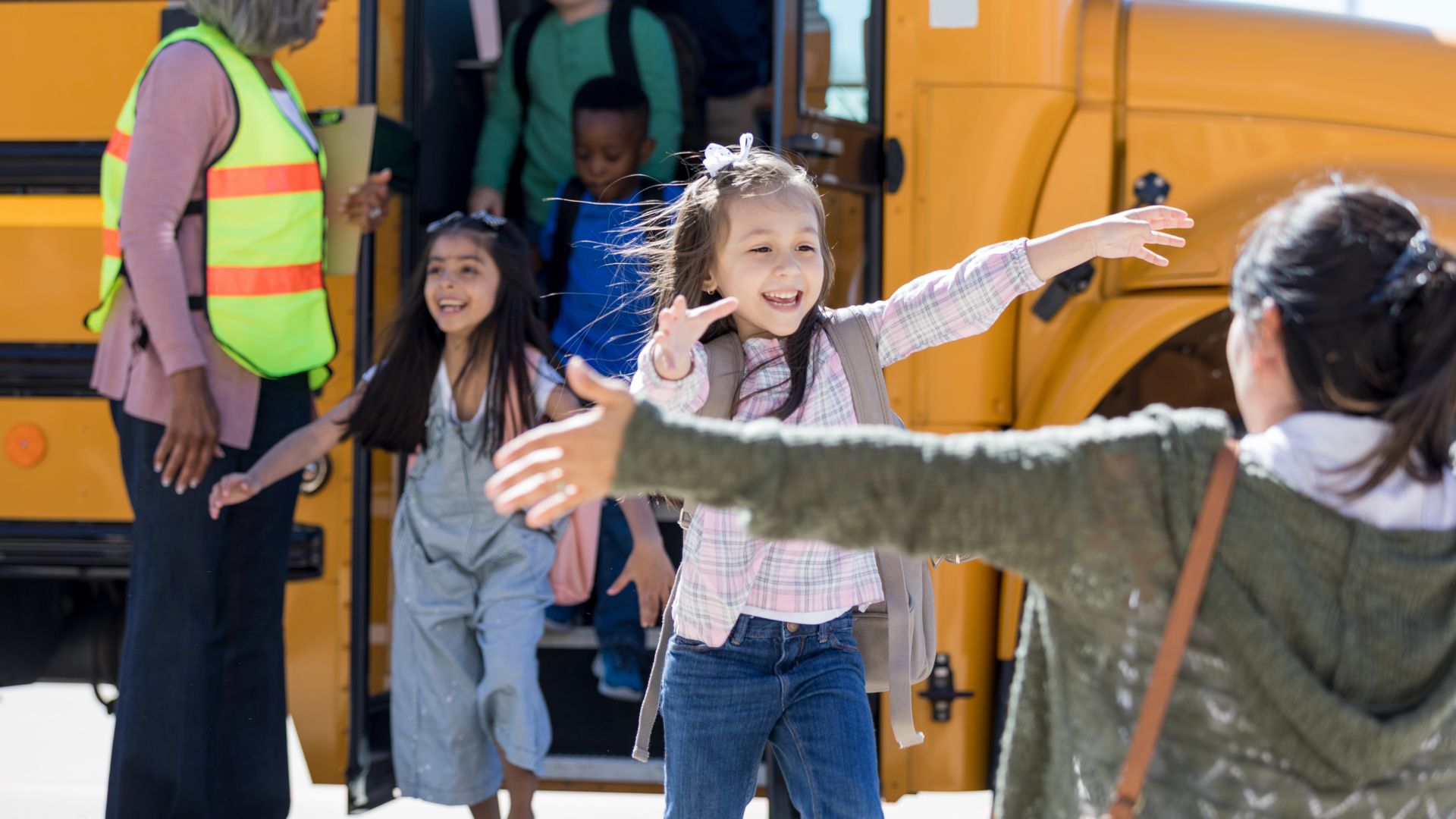 Excited little girl runs into her mother's waiting arms after her first day of kindergarten.