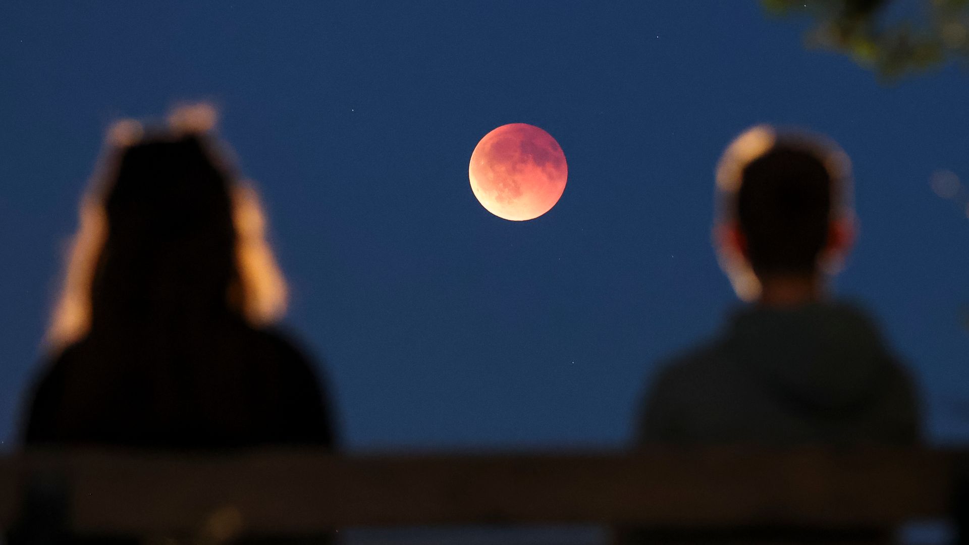 Onlookers watch the total lunar eclipse, also known as the blood moon, from a park bench. The moon gradually moves into the Earth's shadow - until it becomes a total lunar eclipse.