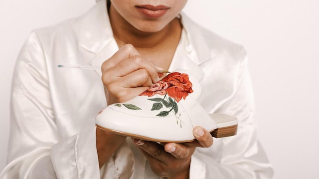 woman painting red roses on white mules