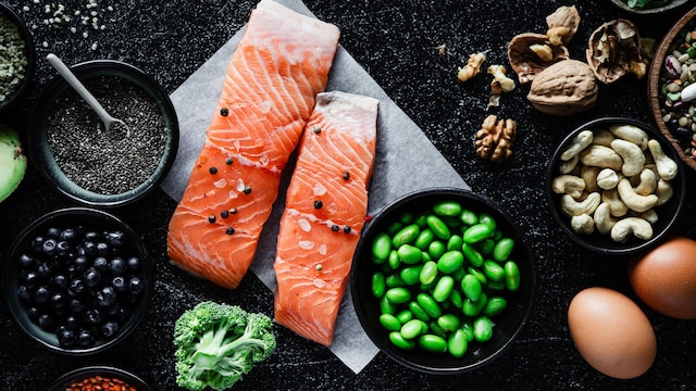 Table top view of Omega 3 rich food items on black background. Fresh raw salmon steak with beans, broccoli, lentil seeds, blueberries, chia seeds, walnuts, cashews, and brown eggs on black kitchen table. 
