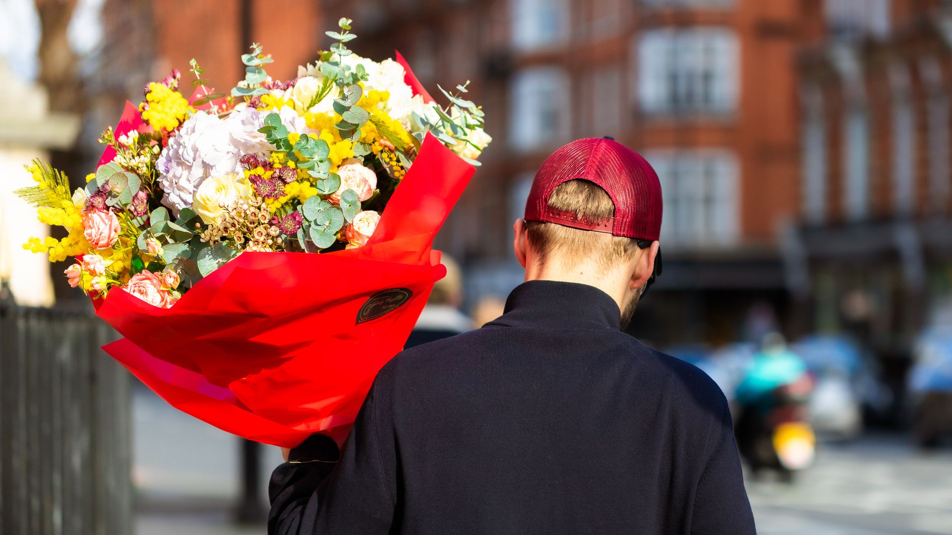 London, UK - 14 February, 2026: close up image depicting the rear view of a young man carrying a bouquet of fresh flowers on a city street in central London on Valentine's Day. 
