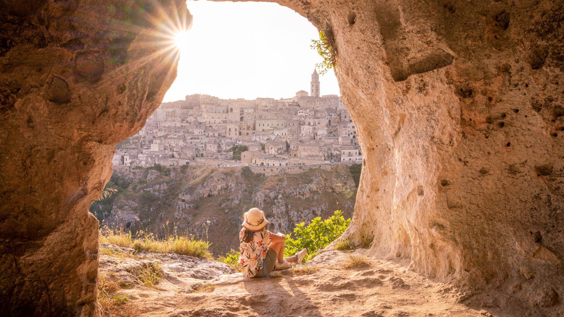 Tourist woman admiring Matera from a cave at sunset, Basilicata, Italy. Sunburst. European Capital of Culture 2019
