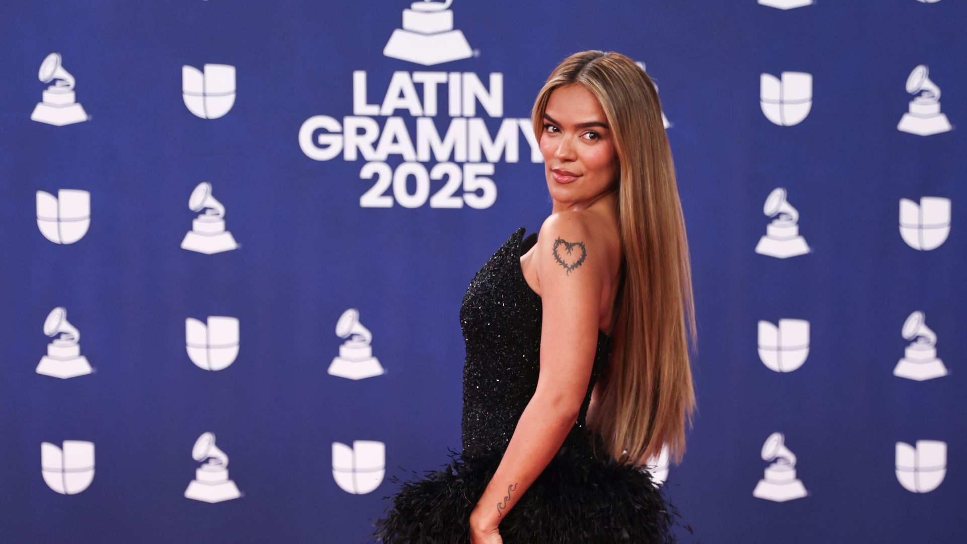 Karol G turns heads in dramatic black feathered gown with emerald accessories at the Latin Grammys