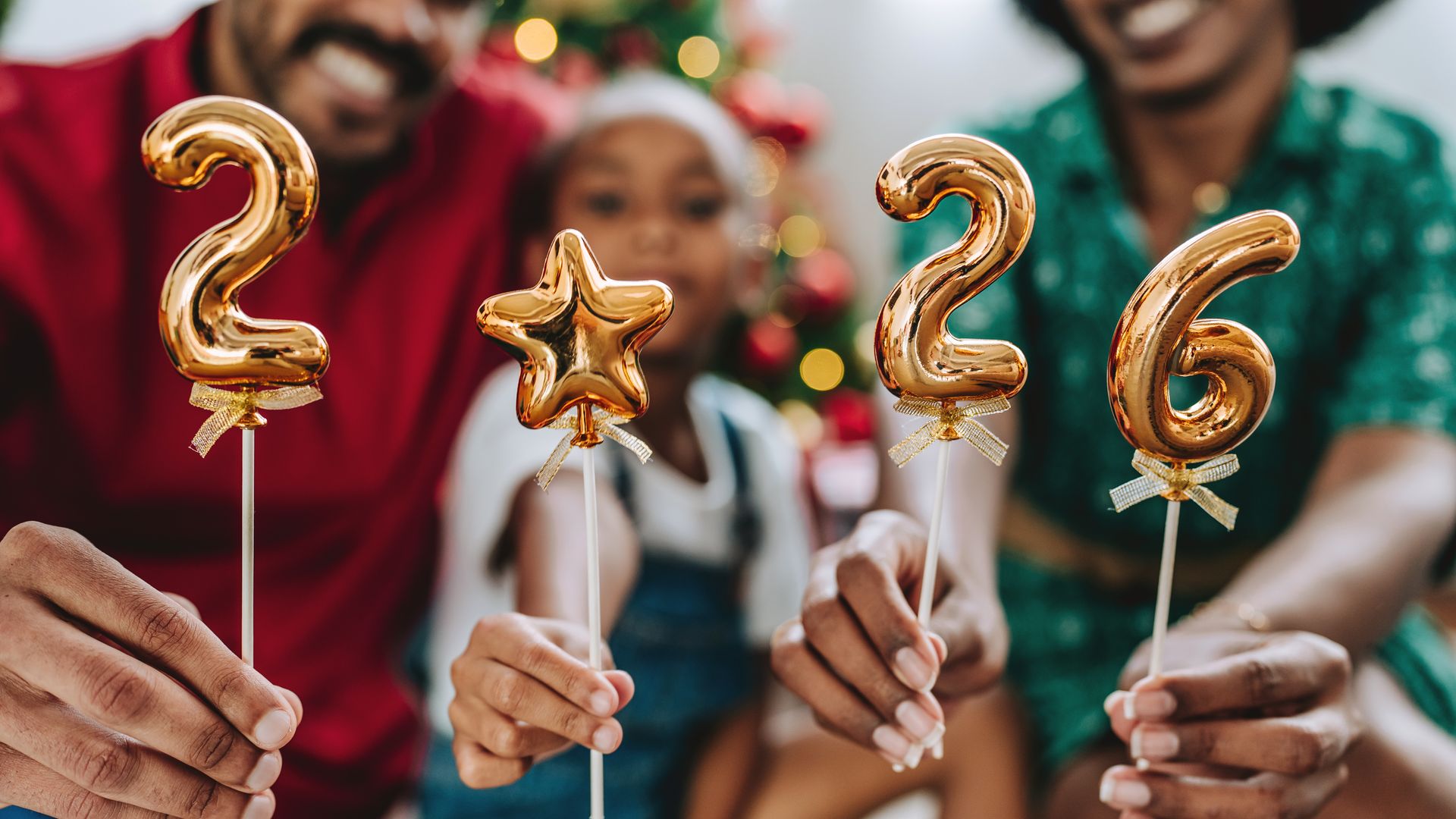 Festive family celebrating the new year at home, holding golden balloons with the numbers 2026. Christmas tree and holiday decorations in the background, joyful and warm atmosphere. Concept of family togetherness, holidays, festive season, new beginnings, 2026 celebration 