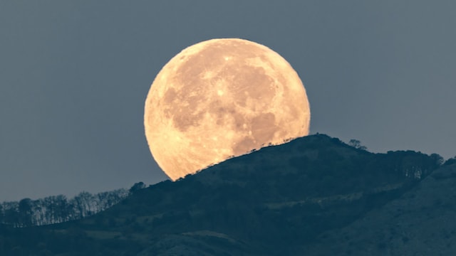 The full moon disappears behind the mountains, casting a serene and ethereal light over the landscape. Nature's quiet spectacle unfolds as the moon bids its silent farewell against the backdrop of the waking world.