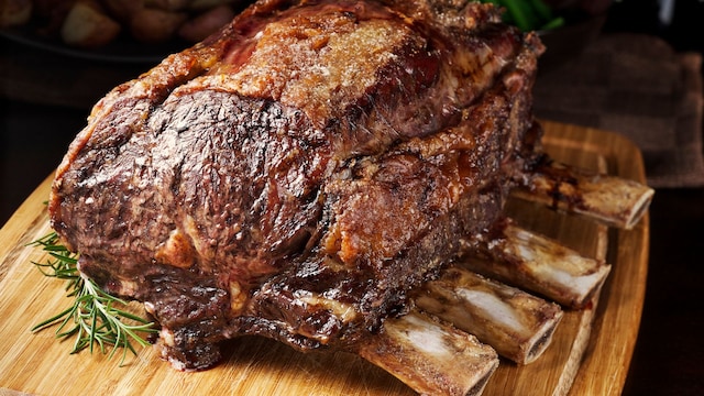"SEVERAL MORE IN THIS SERIES. Roasted prime rib, hot from the oven, dripping juices, and ready to be carved.  Also known as a standing rib roast; this is the cut from which ribeye steaks are made.  Potatoes, green beans and wine bottle in the background.  Shallow DOF." 