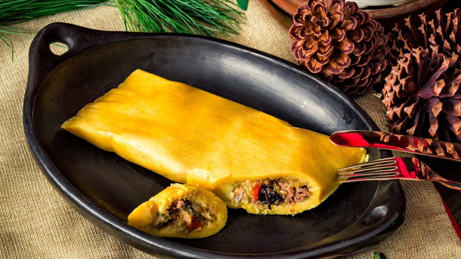 Venezuelan traditional Christmas food: Hallacas on rustic dish.
Hallaca is a traditional and original dish of the Venezuelan cuisine. It is made of beef, pork, chicken and mixed with raisins, olives, peppers, onions, capers, and olives, wrapped in cornmeal dough and folded within plantain leaves. The Hallaca is then tied with strings, and boiled or steamed afterwards. It is typically a Christmas holiday dish and requires a very elaborated process that is normally made with a family meeting.