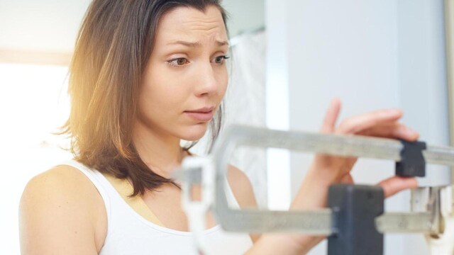 Shot of a young woman weighing herself on a scale