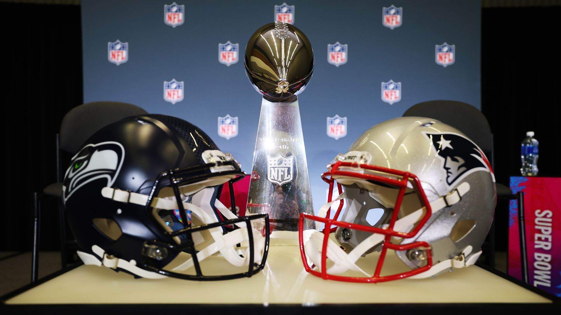 The Vince Lombardi Trophy is framed by the Seattle Seahawks and New England Patriots helmets.