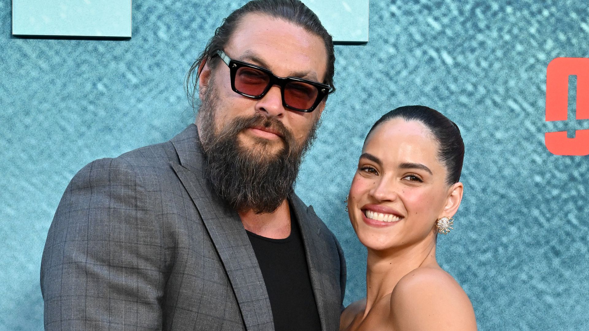 Adria Arjona and Jason Momoa share a sweet kiss on the 'Onslaught' red carpet