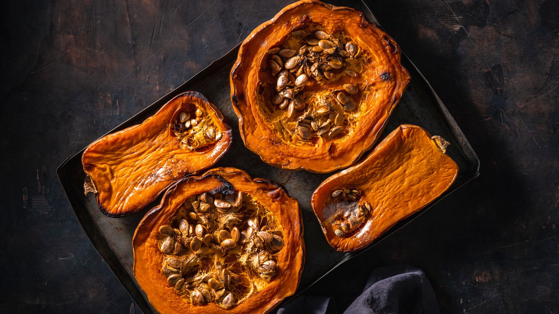 Pumpkin and butternut squash roasted oven on dark wooden background with linen napkin and copy space 