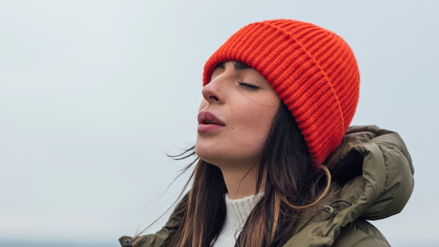 A medium close up of a young woman enjoying a coastal. She is having a mindful moment and doing some breathing exercises and closing her eyes and feeling the sea air on her face. She is in Newton by the Sea in the North East of England. 