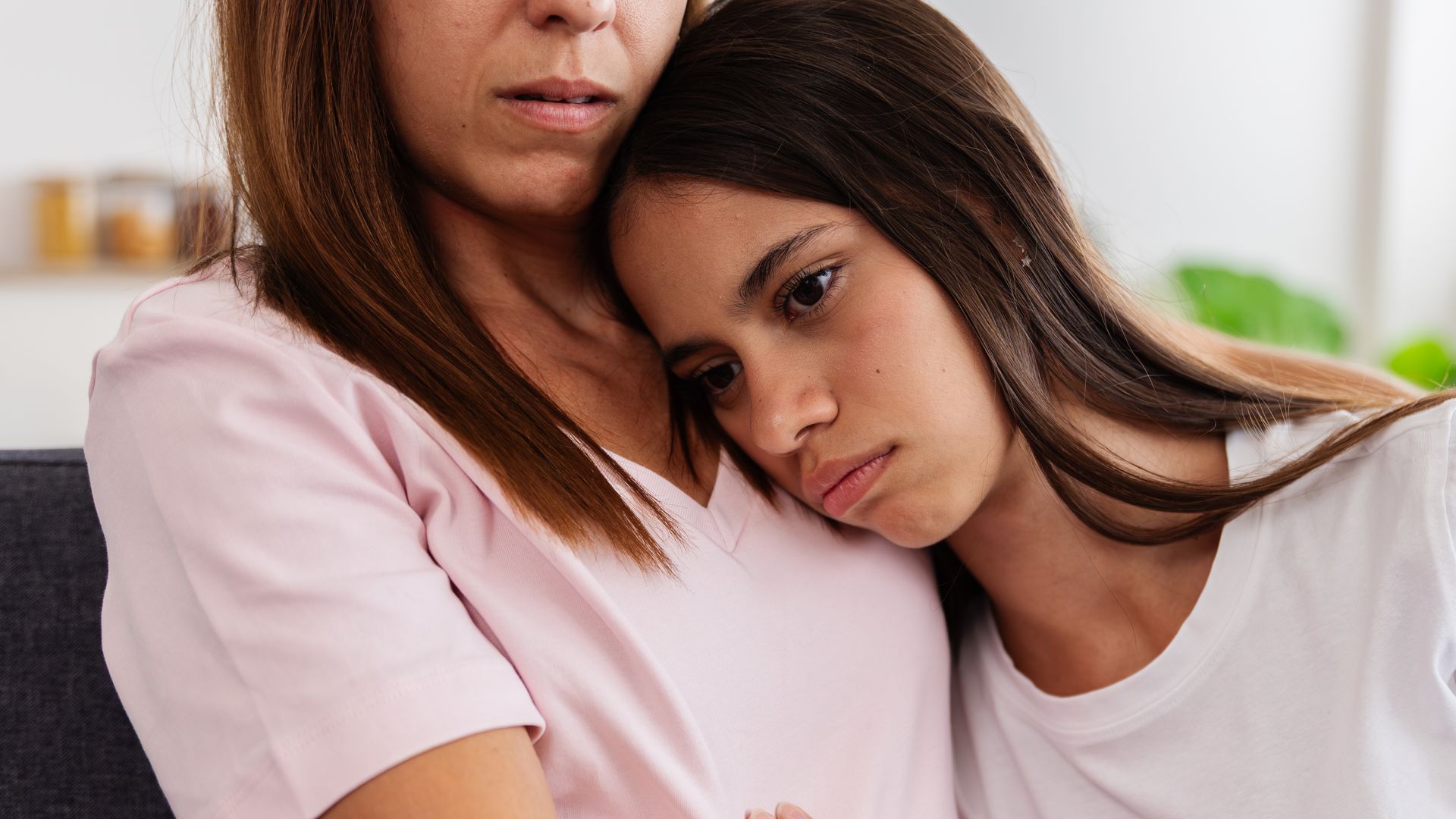 Sad teenage daughter resting head on mother's shoulder, receiving comfort and empathy during a difficult time 