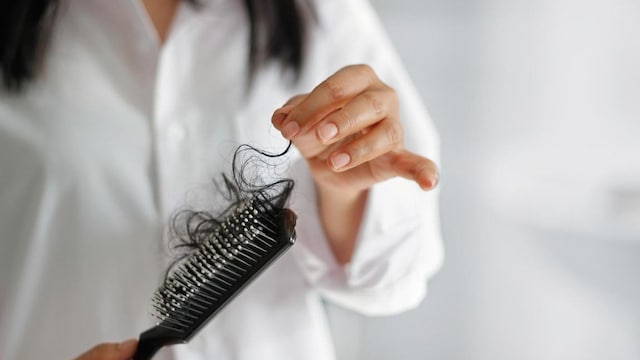 woman losing hair on hairbrush in hand on bathroom background, soft focus