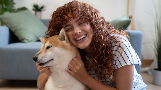 Young redhead woman cuddling her Shiba Inu dog in the living room, showing love and affection   