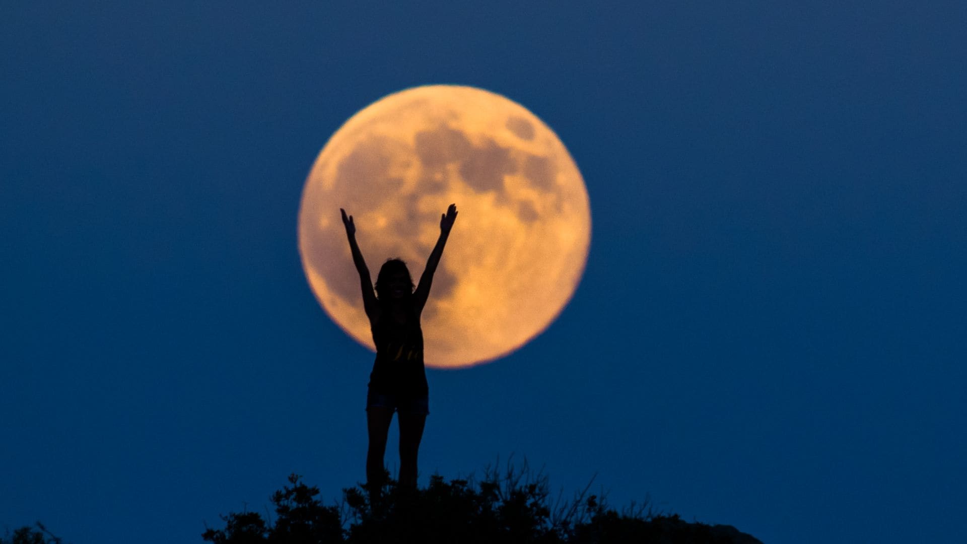 Happy silhouette with arms raised on the full moon woman. The year's biggest moon, in Benicassim, Castellon.