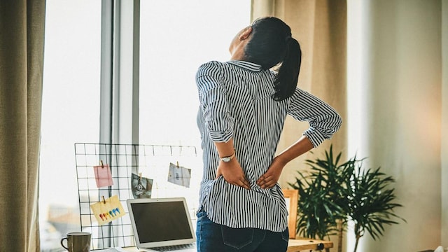 Rearview shot of a young woman suffering with back pain while working from home