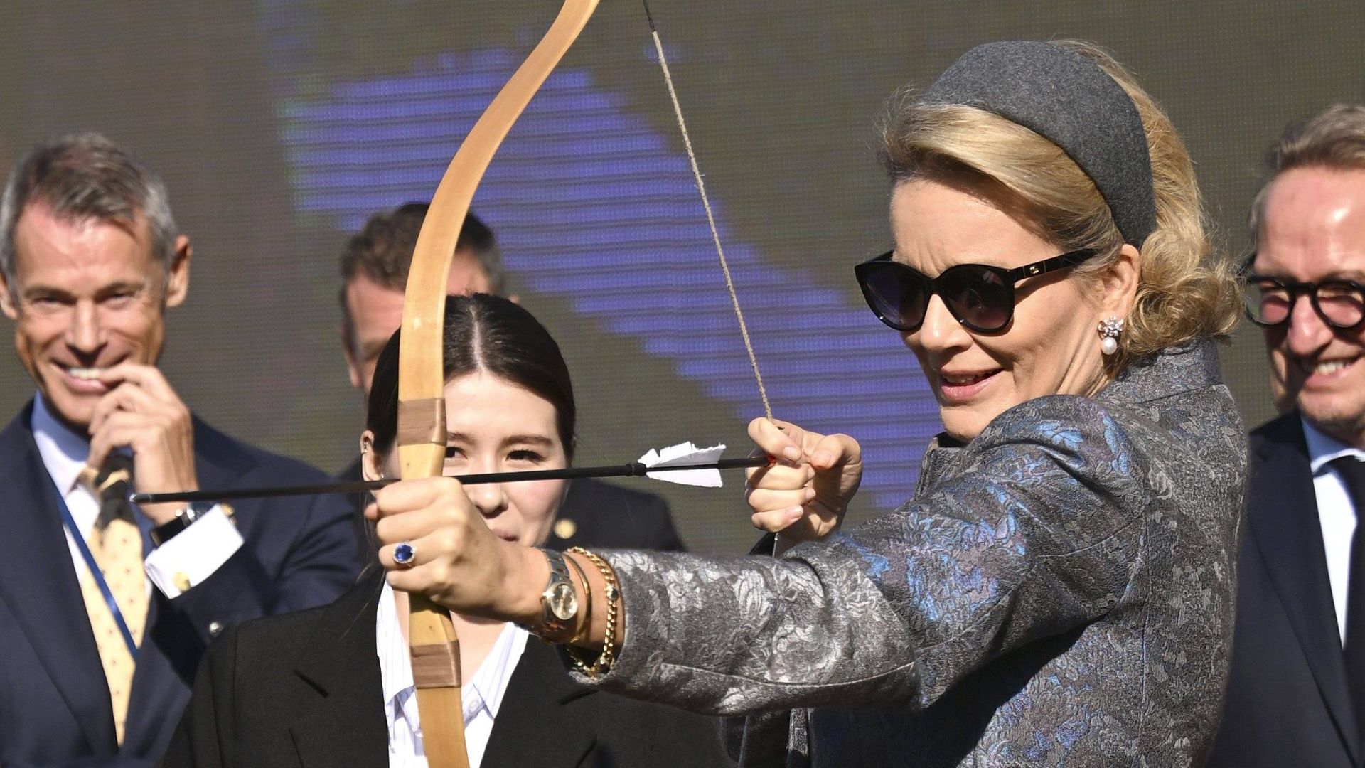 Queen Mathilde tries archery in heels and an elegant floral coat as King Philippe watches with a smile