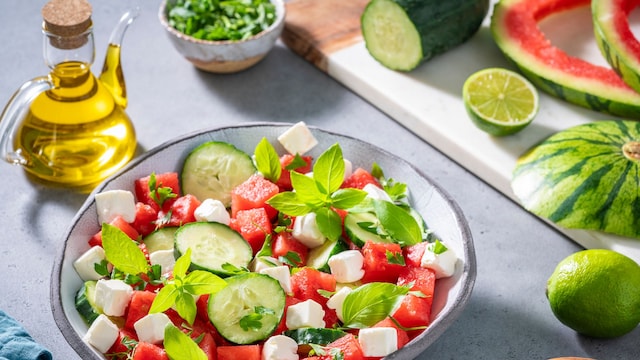 Healthy vegetarian watermelon salad bowl with feta cheese, cucumber and parsley on gray background with cutting board and olive oil, Mediterranean diet 