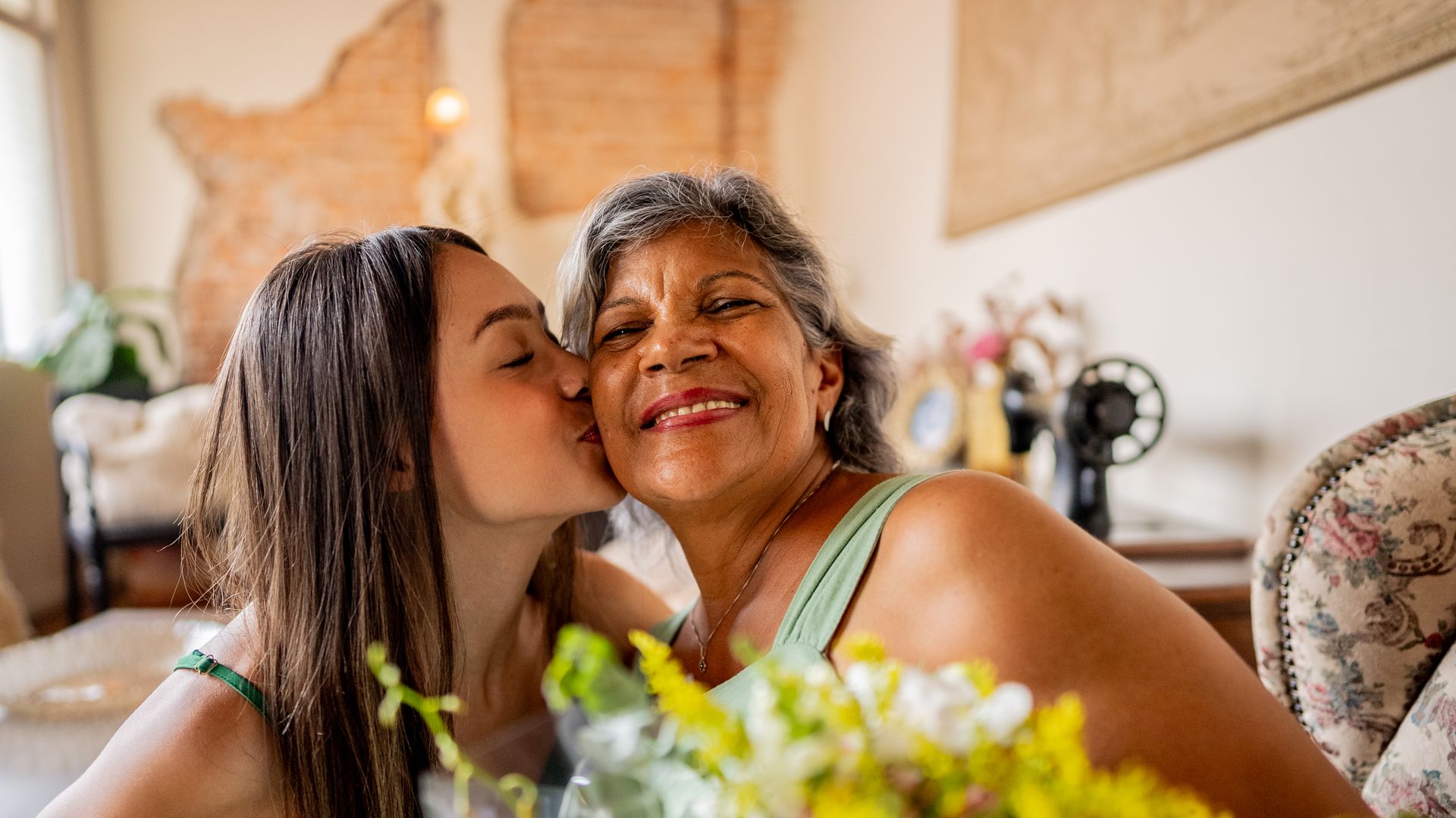 Young woman giving flowers to grandmother at home