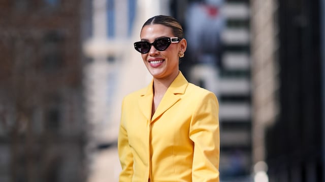 Michelle Salas wears sunglasses, a yellow oversized blazer jacket, a green leather bag/clutch, a tulle pleated/gathered long skirt, high heels, and pointed shoes/pumps outside Carolina Herrera during New York Fashion Week on February 12, 2024, in New York City. 