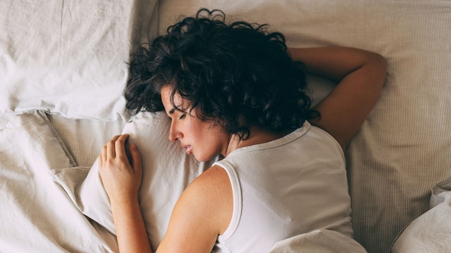 A woman with curly hair peacefully sleeping in a cozy bed, showcasing relaxation and restfulness. Perfect representation of comfort and tranquility for a restful night. 