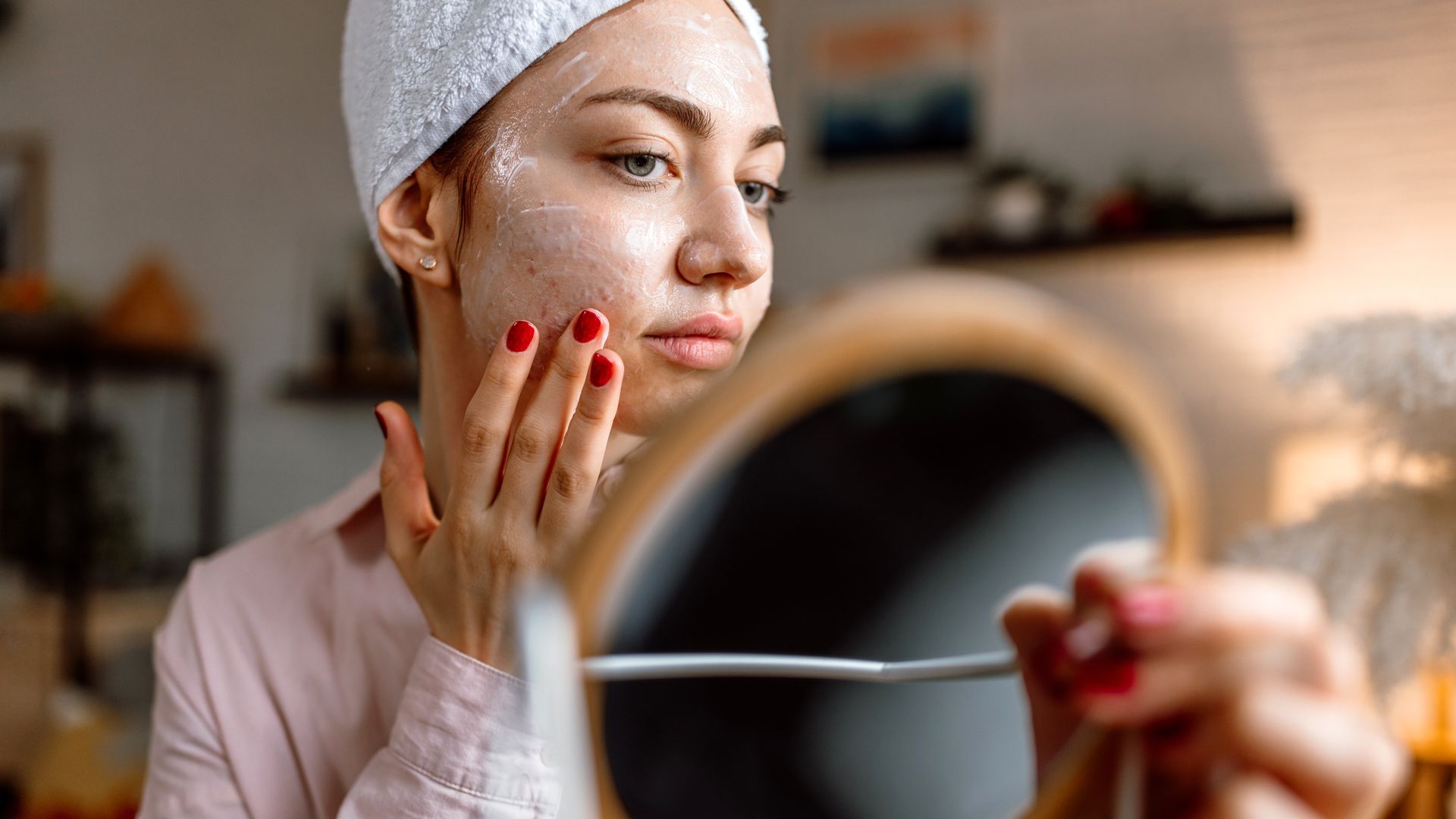Young woman with problematic skin holding a mirror and doing her face care routine. 