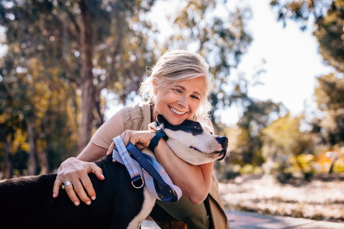  Happy senior woman enjoying walk in nature and embracing pet dog in forest park