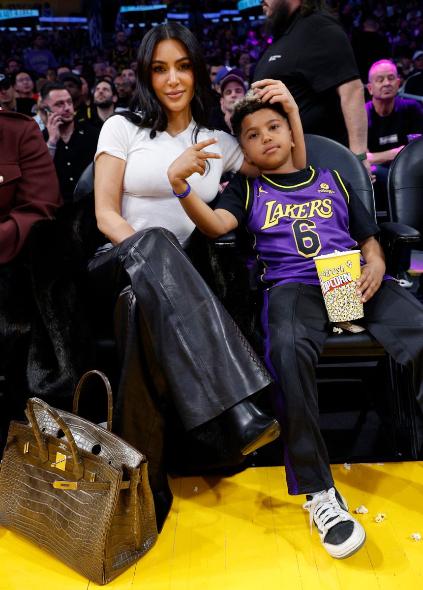 Kim Kardashian and a young boy in Lakers jersey sitting at a basketball game, holding popcorn.