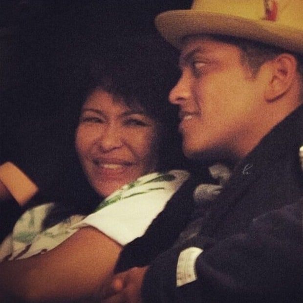 Bruno Mars and a woman smiling together, wearing a yellow hat and a green shirt.